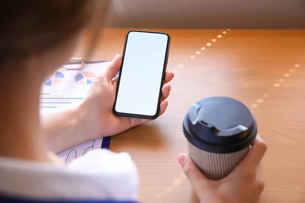 オフィスのテーブルで携帯電話とコーヒーのカップを持つ女性 クローズアップ — ストック写真