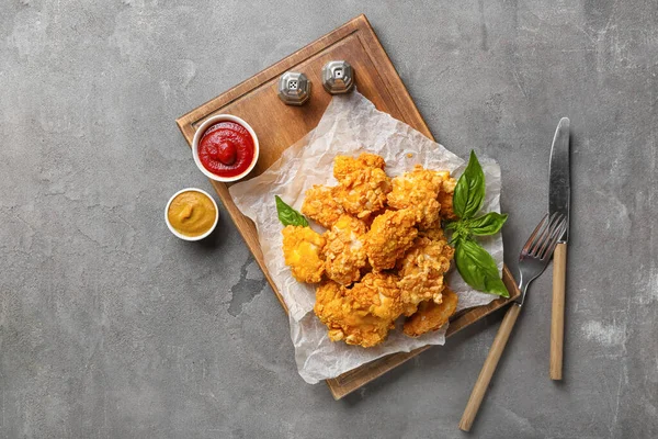 Board with tasty popcorn chicken, sauces and spices on grey background
