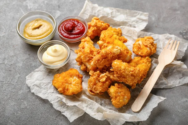 Parchment with tasty fried popcorn chicken and sauces on grey background