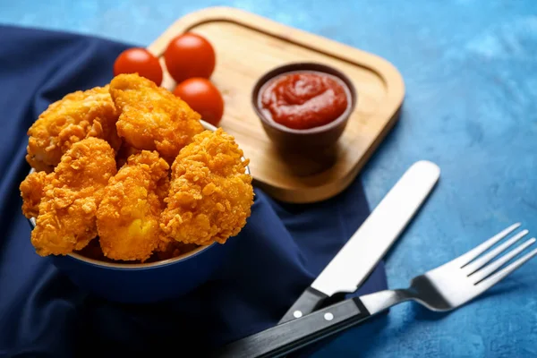 Bowl with tasty fried popcorn chicken and tomato sauce on color background, closeup
