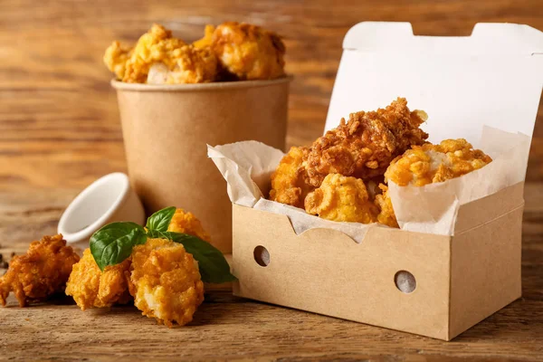 Paper box and bucket with popcorn chicken on wooden background, closeup