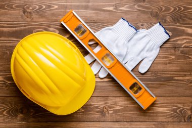 Ahşap arka planda sert şapka, eldiven ve inşaatçı düzeyi