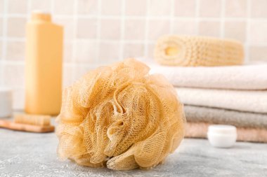 Yumuşak banyo süngeri, duş jeli şişesi ve havlular masanın üstünde.