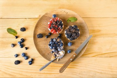 Tahta arka planda kaşık ve lezzetli meyveli tartlarla dolu bir tabak.