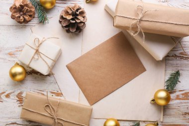 Beyaz ahşap arka planda Noel topları, hediyeler ve koniler olan kart