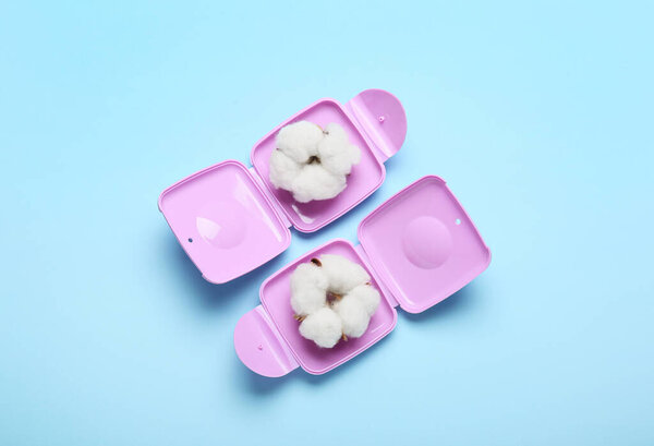 Plastic boxes for storing women's tampons with cotton flowers on blue background