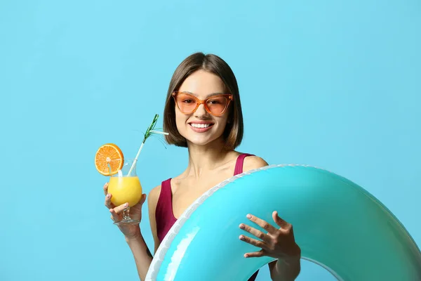 Young woman with cocktail and inflatable ring on color background