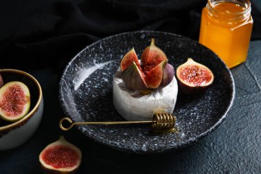 Tabak dolusu peynir, olgun incir ve koyu arkaplanda bal, yakın plan.