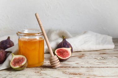 Bal dolu cam kavanoz ve açık ahşap masada olgun incir.