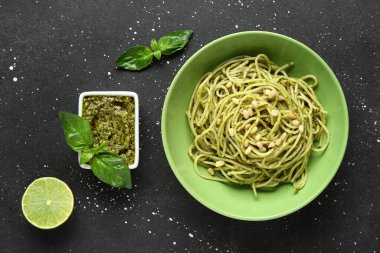 Lezzetli soslu makarna tabağı, bir kase sos ve siyah grunge arkaplanda malzemeler.