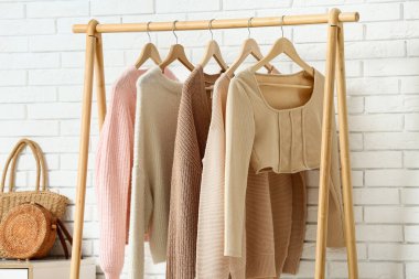 Beyaz tuğla duvarın yanında asılı giysilerle dolu şık bir salonda, yakın plan.