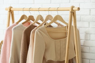 Beyaz tuğla duvarın yanında asılı giysilerle dolu şık bir salonda, yakın plan.