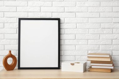 Kitaplar, vazo ve beyaz tuğla duvarın yanındaki boş çerçeve.