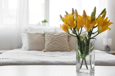 Yatak odasındaki komodinin üzerinde güzel zambak çiçekleri olan vazo, yakın plan.