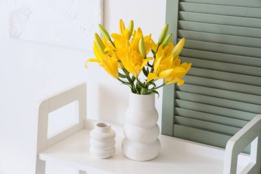 Beyaz duvarın yanındaki raflarda güzel zambak çiçekleri olan vazo.