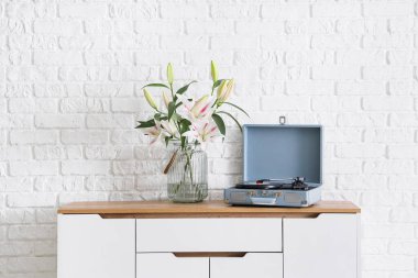 Güzel çiçekli vazo ve beyaz tuğla duvarın yanındaki dolapta kayıt cihazı.