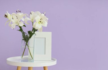 Üzerinde güzel zambak çiçekleri ve çerçeve olan vazo eflatun duvarın yanında.