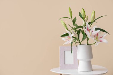 Güzel çiçekli vazo ve bej duvarın yanındaki sehpanın üzerindeki çerçeve.
