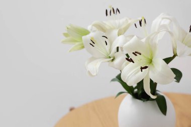 Beyaz duvarın yanında, sehpanın üzerinde güzel çiçekli vazo, yakın plan.