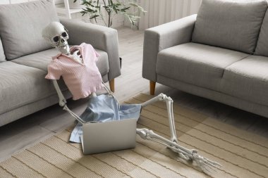 Oturma odasındaki kanepenin yanında dizüstü bilgisayarı olan iskelet.