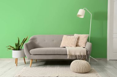 Yeşil duvarın yanında rahat gri kanepesi ve standart lambası olan şık bir oturma odası.