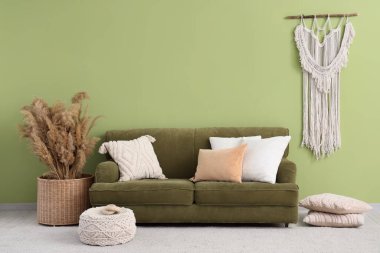 Yeşil duvarın yanında rahat kanepesi ve otları olan şık bir oturma odası.