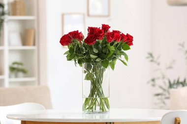 Süslü oturma odasında beyaz sehpanın üzerinde kırmızı güller olan bir vazo.