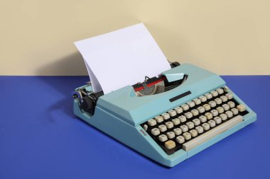 Mavi masada bej duvara karşı boş kağıt kağıtlı klasik daktilo
