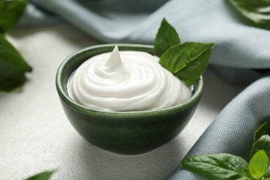 Lezzetli ekşi kremalı kase ve beyaz grunge masasında taze fesleğen.