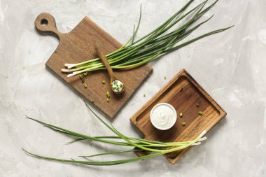 Tabak ve kaşık dolusu ekşi krema ve grunge masasında doğranmış yeşil soğan dilimleme tahtaları.