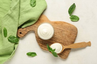 Kase ve bir kaşık ekşi krema ve beyaz grunge masasında taze fesleğen ile kesme tahtaları.