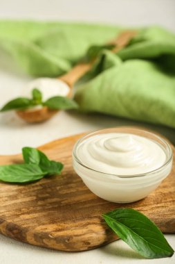 Lezzetli ekşi krema ve beyaz grunge masasında taze fesleğenle kesme tahtası.