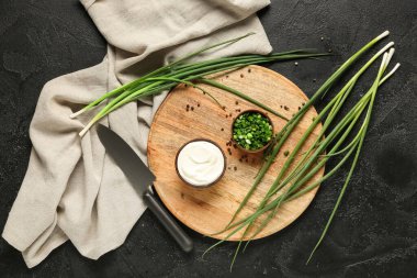 Lezzetli ekşi krema, yeşil soğan, karabiber ve siyah grunge masasında bıçak.