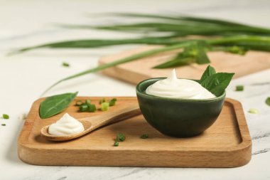 Kase ve bir kaşık ekşi krema ve beyaz mermer masada taze fesleğenle kesme tahtası.