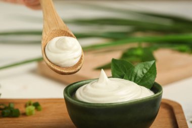 Kase ve bir kaşık ekşi krema ve beyaz mermer masada taze fesleğenle kesme tahtası.