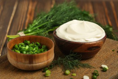 Bir kase taze dereotlu ekşi krema ve ahşap masada doğranmış yeşil soğan. Yakın plan.