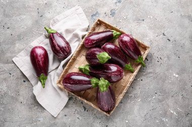 Gri arka planda taze olgun patlıcan dolu hasır tepsi.