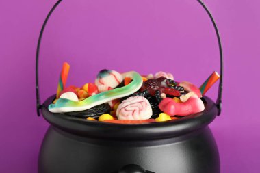 Mor arka planda farklı tatlı Cadılar Bayramı jeli şekerlerinden oluşan bir kazan, yakın plan.