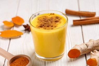 Bir bardak sağlıklı zerdeçal ve beyaz ahşap arka planda malzemeler, yakın plan.