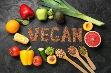 Meyveli farklı taze sebzeler ve grunge siyah arka planda karabuğdaydan yapılmış VEGAN kelimesi.