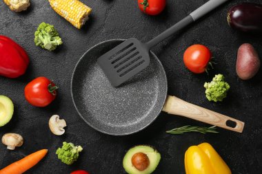 Spatulalı kızartma tavası ve grunge siyah arka planda farklı taze sebzeler. Dünya Vejetaryen Günü