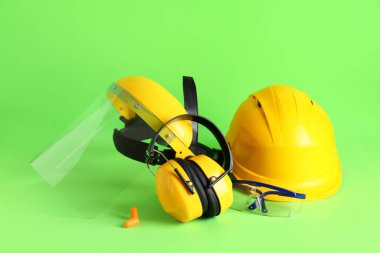 Sert şapka, koruyucu kulaklık ve yeşil arka planda yüz kalkanı.