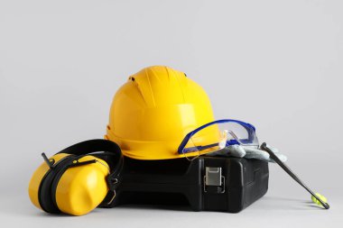 Sert şapka, koruyucu kulaklıklar ve gri arka planda alet çantası.
