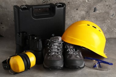 Gri grunge arka planda sert şapka, bot, koruyucu kulaklık ve alet çantası.