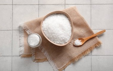 Hafif fayans zemininde bir kase deniz tuzu, kaşık ve peçeteyle kompozisyon