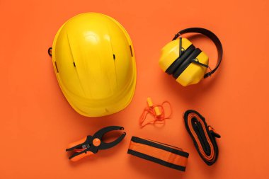 Sert şapka, koruyucu kulaklık ve turuncu arka planda güvenlik ekipmanı.