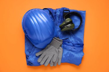 Sert şapka, koruyucu kulaklık ve turuncu arka planda güvenlik ekipmanı.