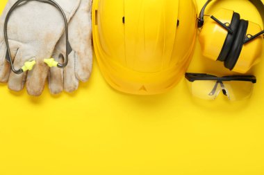 Sarı arka planda sert şapka, eldivenler ve güvenlik gözlükleri.