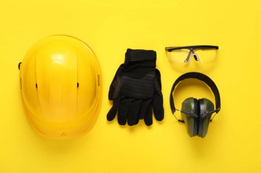 Sert şapka, koruyucu kulaklıklar, güvenlik gözlükleri ve sarı arka planda eldivenler.