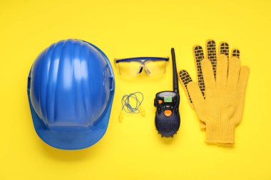 Sert şapka, radyo vericisi, sarı arka planda eldivenler ve güvenlik gözlükleri.